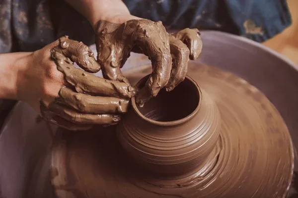 Hands shaping a clay vessel on a pottery wheel